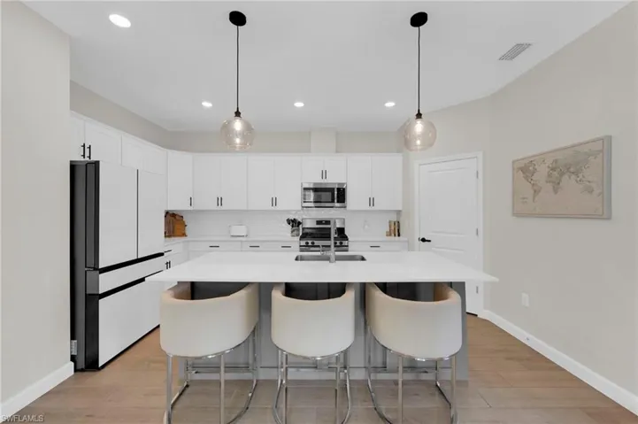 Kitchen with stainless steel appliances, hanging light fixtures, an island with sink, a breakfast bar area, and recessed lighting