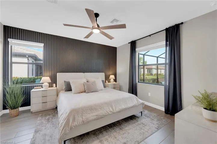 Bedroom featuring an accent wall, multiple windows, a ceiling fan, and wood finished floors