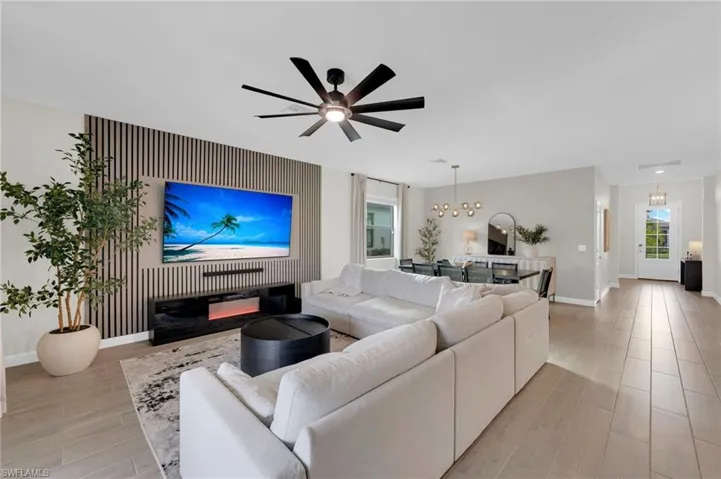 Living room with wood finish floors, a chandelier, an accent wall, a ceiling fan, and a glass covered fireplace