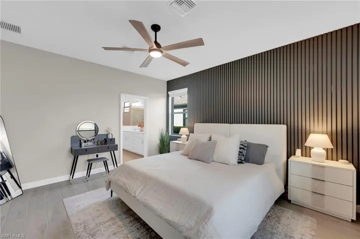 Bedroom featuring an accent wall, light wood-style flooring, a ceiling fan, and ensuite bathroom