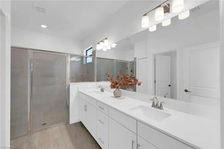 Full bathroom featuring double vanity, a stall shower, and light wood finished floors