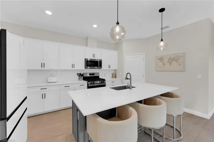 Kitchen featuring appliances with stainless steel finishes, white cabinetry, a kitchen island with sink, pendant lighting, and backsplash