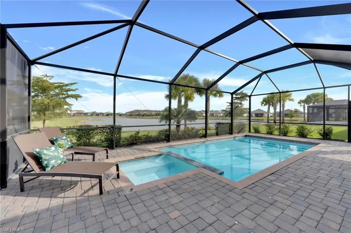 View of pool with a sunroom, a pool with connected hot tub, a water view, a lanai, and a patio area