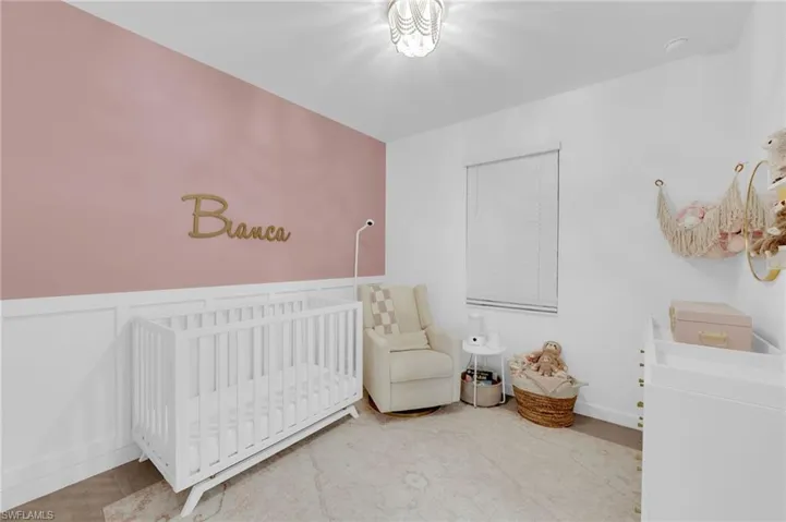Bedroom featuring a nursery area, a wainscoted wall, and a decorative wall