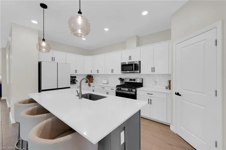 Kitchen with appliances with stainless steel finishes, white cabinets, pendant lighting, an island with sink, and backsplash