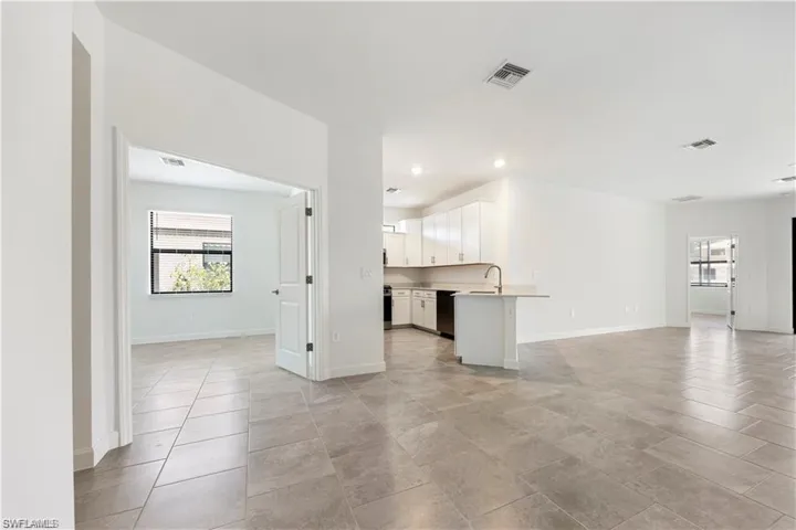 Open-concept living space featuring light-toned tile flooring, recessed lighting, and a kitchen with white cabinetry and stainless steel appliances