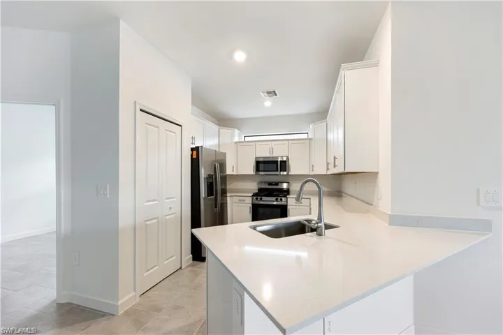 Contemporary kitchen featuring white cabinetry, stainless steel appliances, a stainless steel sink with a gooseneck faucet, and light-toned countertops