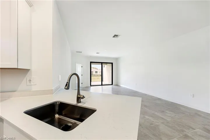 Stainless steel sink with a pull-down faucet, light-toned countertop, white cabinetry, and gray tile flooring