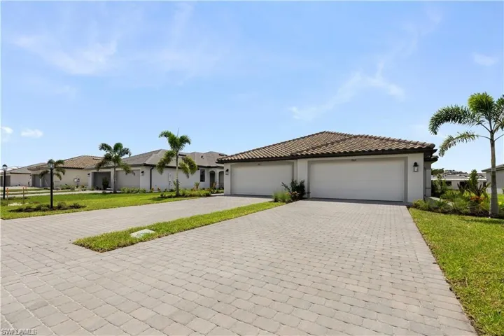 Paver driveway, two-car garage, tile roof, stucco exterior, and manicured landscaping with palm trees
