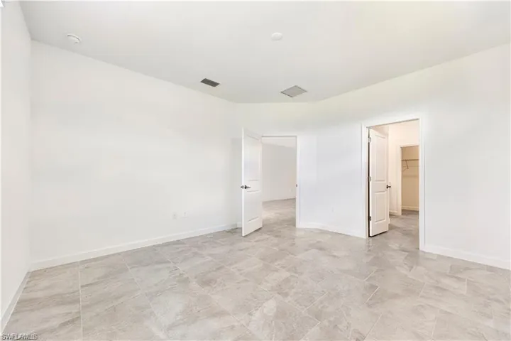 Spacious room featuring neutral tile flooring, white walls, and multiple doorways