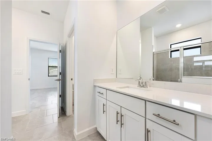 Spacious vanity featuring double sinks with chrome fixtures, an expansive mirror, white cabinetry, and light-toned flooring