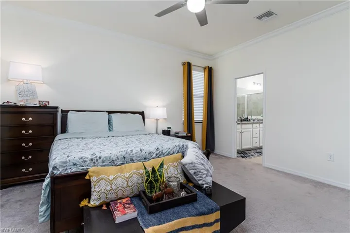 Carpeted bedroom with ceiling fan, ensuite bath, and crown molding