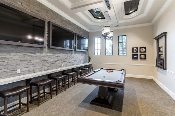 Rec room with dark colored carpet, pool table, crown molding, and bar area