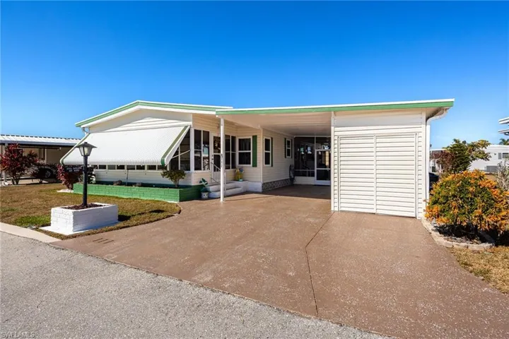 Manufactured / mobile home featuring an attached carport, a front yard, and concrete driveway