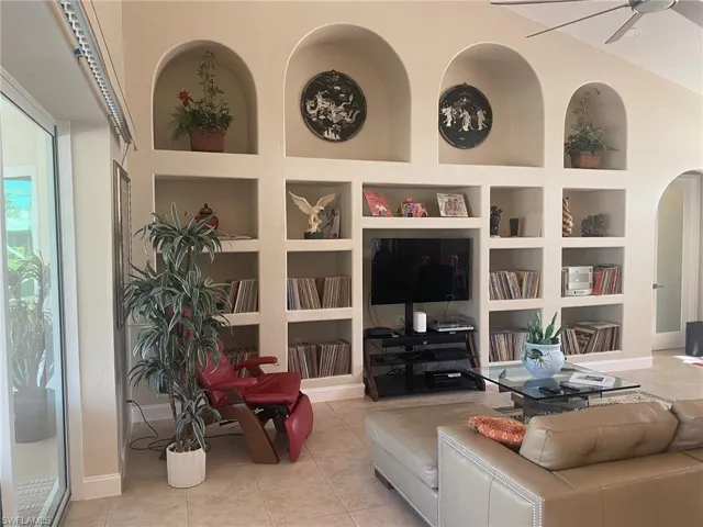 Tiled living room featuring ceiling fan, built in features, and lofted ceiling