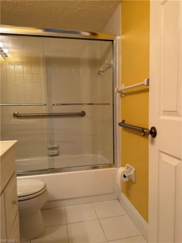 Full bathroom featuring a textured ceiling, tile patterned flooring, vanity, and bath / shower combo with glass door