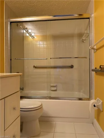 Full bathroom with a textured ceiling, tile patterned flooring, vanity, and combined bath / shower with glass door