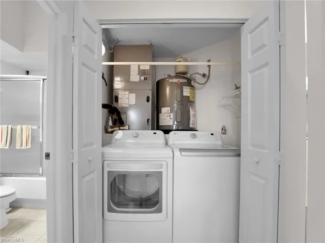 Clothes washing area with washer and dryer, electric water heater, light tile patterned floors, and heating unit