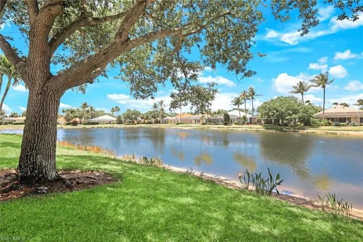 Expansive lakefront property with mature trees, lush green lawn, and tropical landscaping