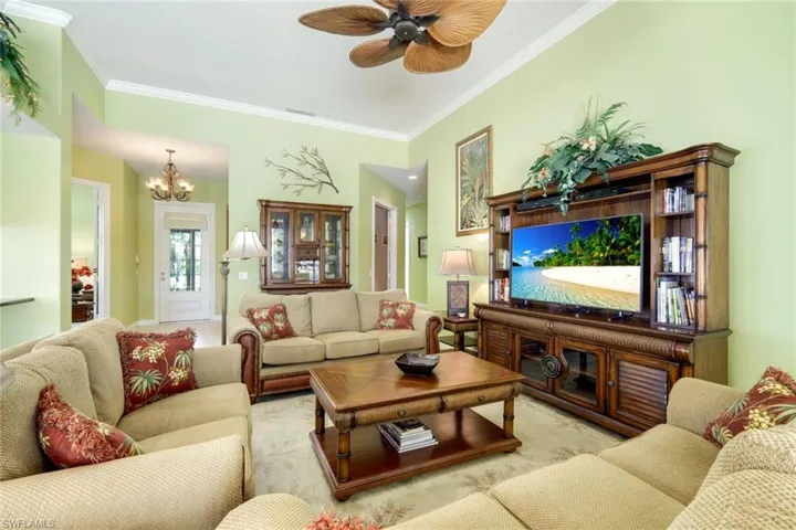 Spacious living area featuring high ceilings with crown molding, a ceiling fan with palm leaf-inspired blades, and a built-in media center with shelving and storage