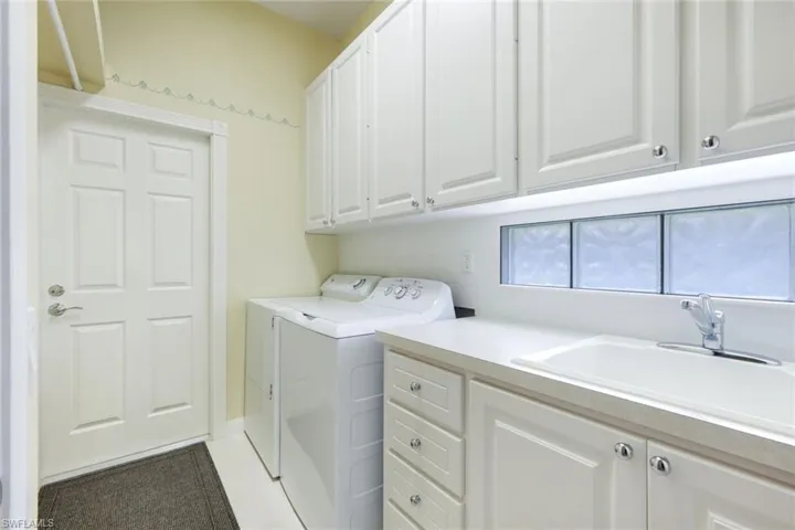 Laundry room featuring white cabinetry, a single basin sink with a chrome faucet, and glass block window accents