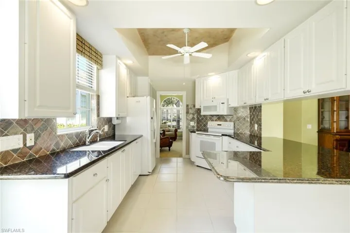 Kitchen featuring white cabinetry, dark granite countertops, tile backsplash, white appliances, and a central ceiling fan