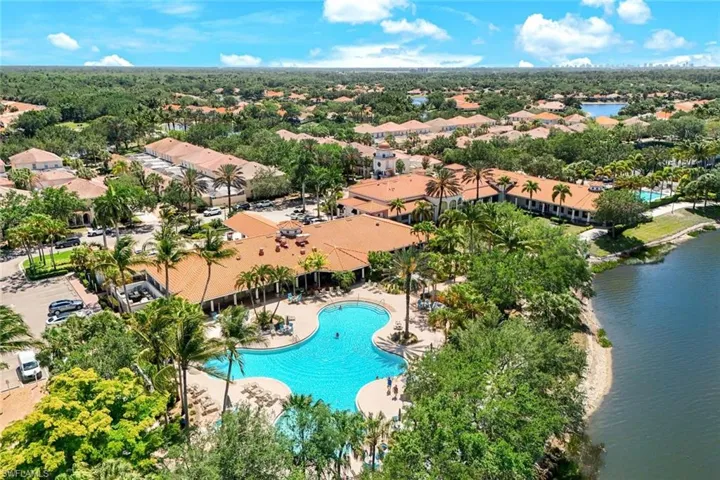 Expansive community featuring a large freeform swimming pool with sun deck, mature palm trees, and terracotta-roofed buildings