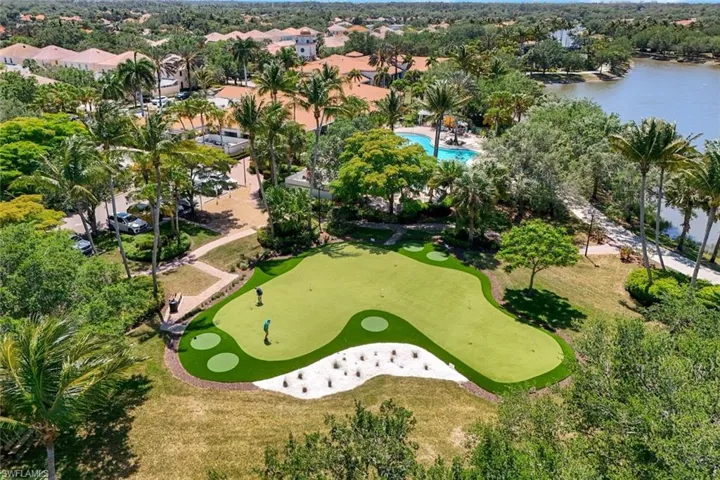 Artificial turf putting green with multiple holes, sand trap, and surrounding landscaping