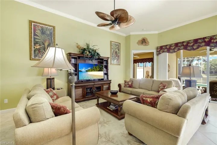 Spacious living area featuring light green walls, crown molding, and a ceiling fan