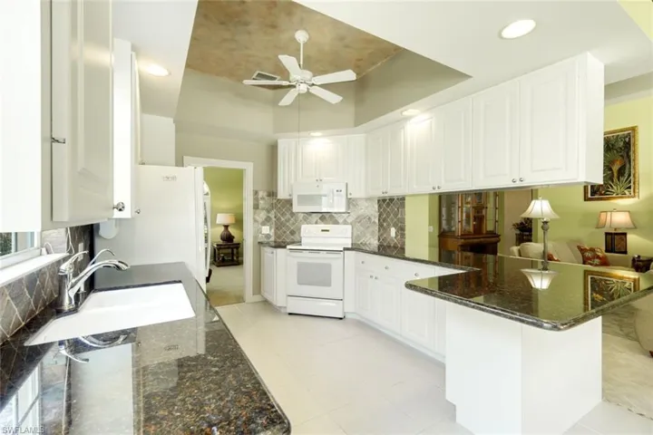 Kitchen featuring white cabinetry, dark stone countertops, tile backsplash, white appliances, and a recessed ceiling with a ceiling fan and recessed lighting