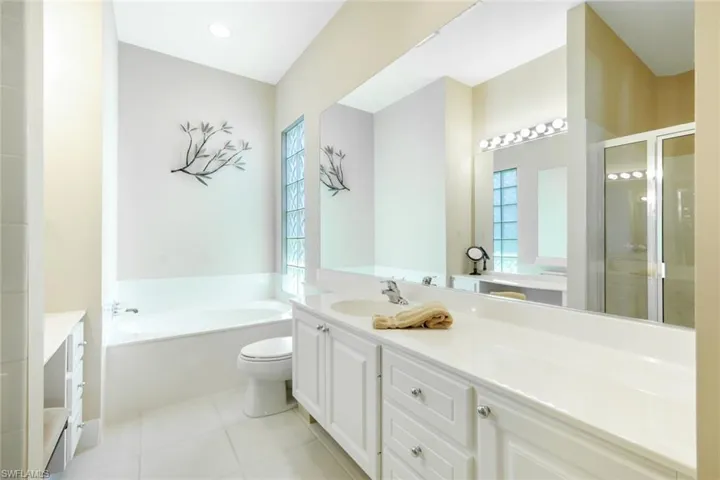 Spacious bathroom featuring a double vanity with white cabinetry, a built-in soaking tub, and a separate glass-enclosed shower