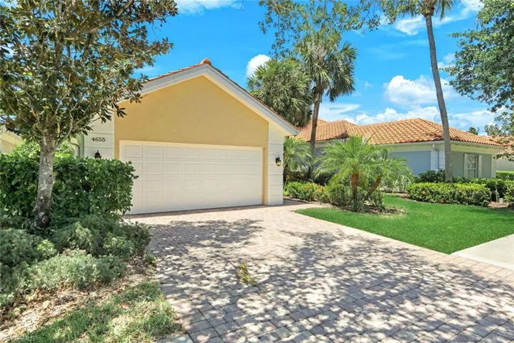 Stucco exterior featuring a two-car garage, concrete tile roof, and paver driveway