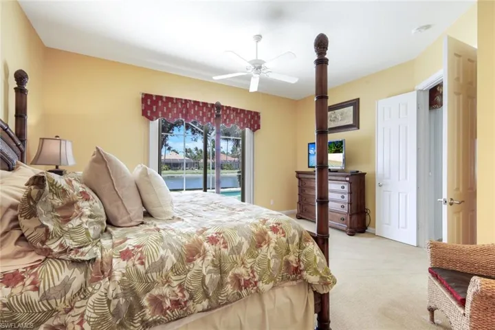 Carpeted bedroom featuring a ceiling fan, light yellow wall color, and a large sliding glass door with a custom valance
