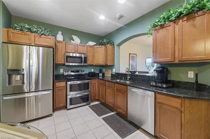 Kitchen featuring stainless steel appliances, dark stone countertops, wood finish cabinets, light tile patterned floors, and arched walkways