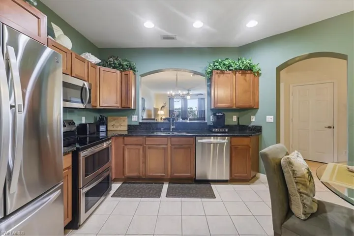 Kitchen featuring stainless steel appliances, dark stone countertops, a chandelier, wood finish cabinetry, and light tile patterned floors