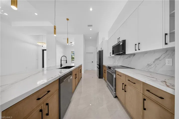 Kitchen with stainless steel appliances, backsplash, glass insert cabinets, light stone counters, and white cabinetry
