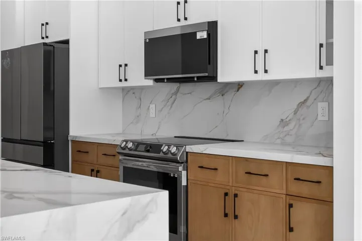 Kitchen featuring hanging light fixtures, light stone countertops, decorative backsplash, and glass fronted cabinets