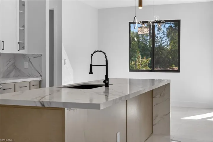 Kitchen featuring a chandelier, light stone countertops, open floor plan, wood finish cabinets, and a kitchen island with sink