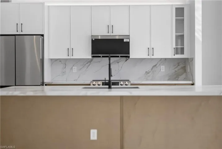 Kitchen with a large island with sink, white cabinetry, stainless steel appliances, a chandelier, and light tile patterned floors