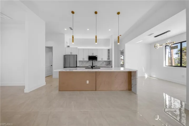 Two tone kitchen featuring stainless steel appliances, decorative light fixtures, dual tone cabinetry, a spacious island, and tasteful backsplash