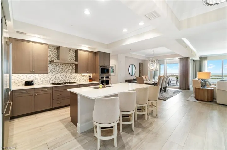Kitchen with wall chimney range hood, stainless steel appliances, a breakfast bar, light wood finished floors, and decorative backsplash