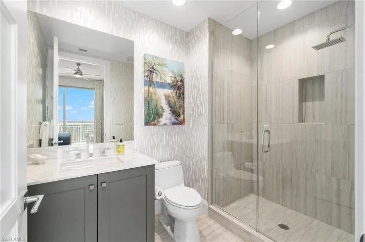 Bathroom with toilet, vanity, a stall shower, wallpapered walls, and ceiling fan