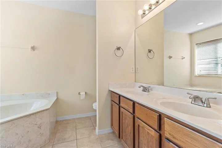 Full bathroom featuring a bath, double vanity, and light tile patterned flooring