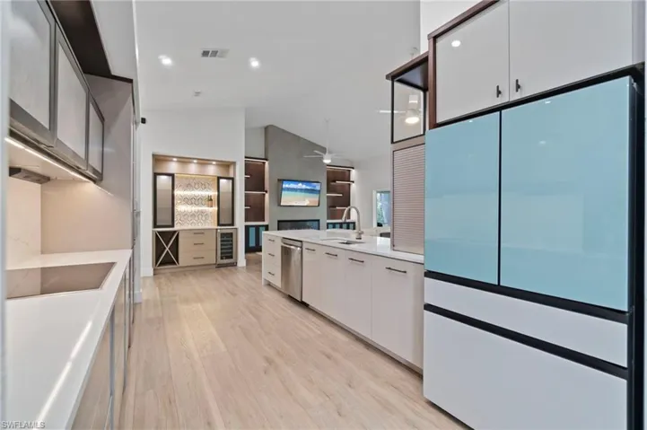 Kitchen featuring freestanding refrigerator, white cabinets, light wood-type flooring, lofted ceiling, and black electric cooktop