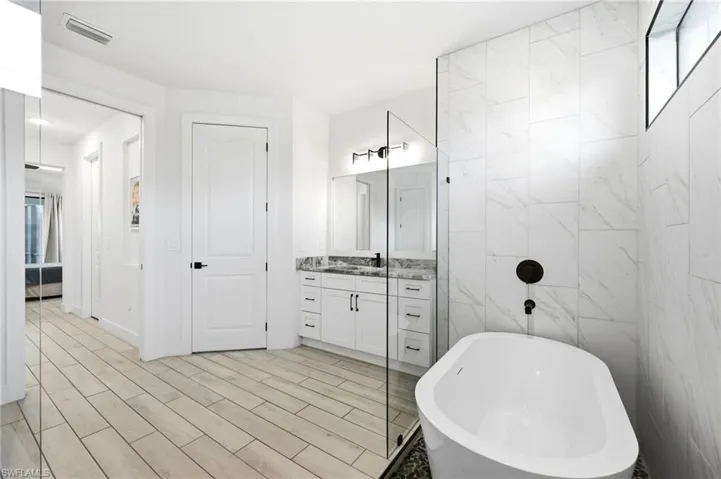 Full bathroom featuring vanity, a freestanding bath, tile walls, wood tiled floors, and a shower