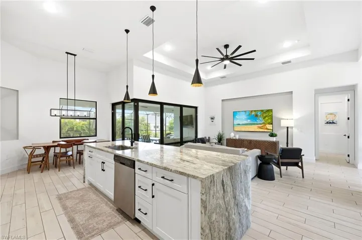 Kitchen with white cabinets, decorative light fixtures, wood tiled floors, light stone counters, and open floor plan
