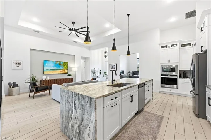 Kitchen with white cabinets, open floor plan, light stone countertops, wood tiled floors, and appliances with stainless steel finishes