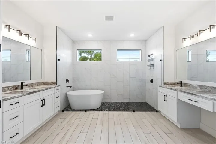 Bathroom with two vanities, a freestanding bath, a walk in shower, and wood tiled floors