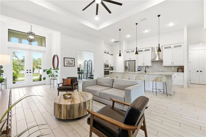 Living room with a towering ceiling, french doors, wood finish floors, ceiling fan, and recessed lighting