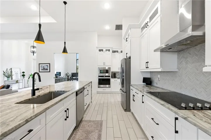 Kitchen featuring wall chimney range hood, white cabinetry, glass insert cabinets, light stone countertops, and recessed lighting
